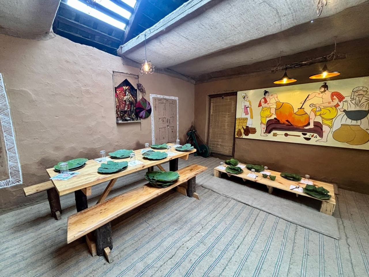 Community dining hall with wooden benches, leaf plates and Chambyali murals at a Khajjiar homestay, Chamba