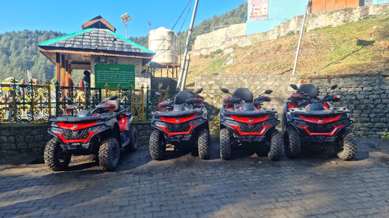 Line of red ATV quad bikes parked by a slate-roof shrine ready for Khajjiar trail rides, Chamba